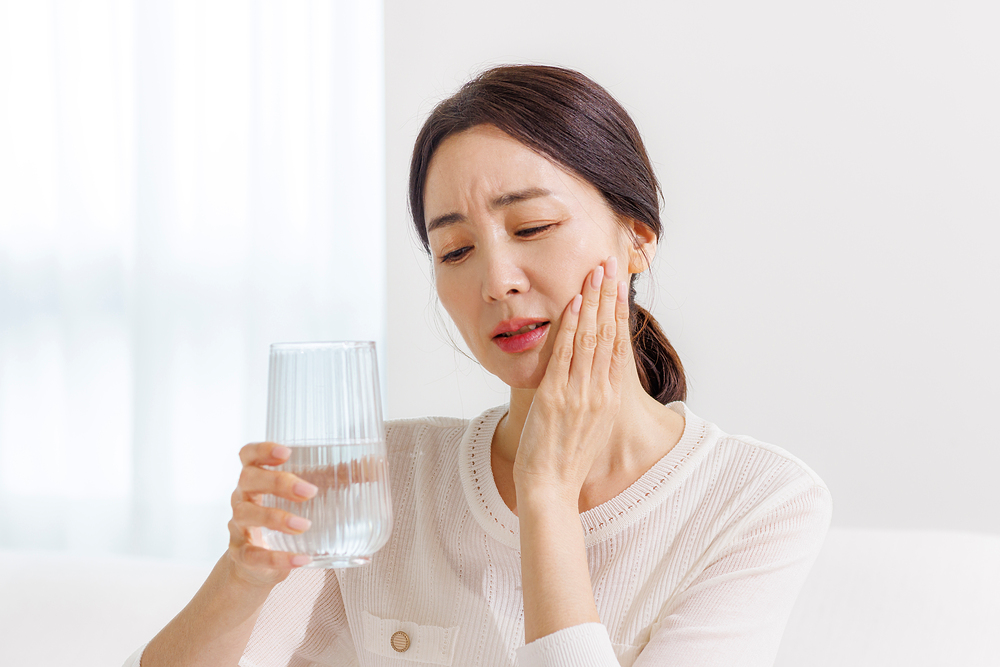 찬물을 마시고 치아가 시려 턱을 감싸는 중년 여성